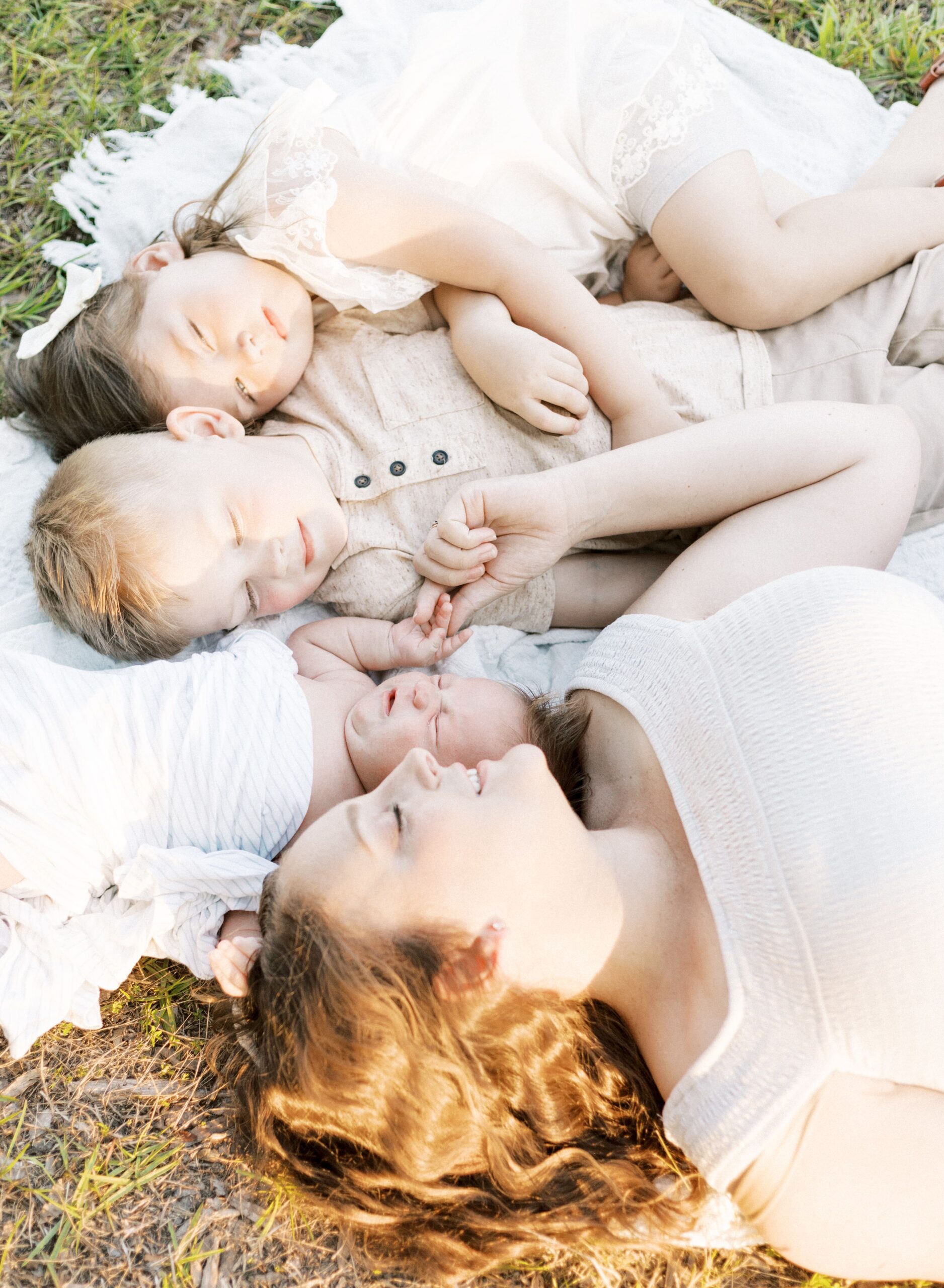 outdoor newborn photos during golden hour with mom, baby, and children laying on blanket