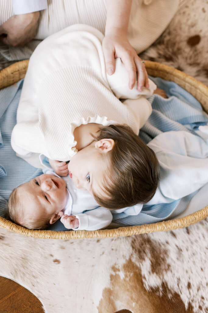 sister hugging newborn baby in bassinet