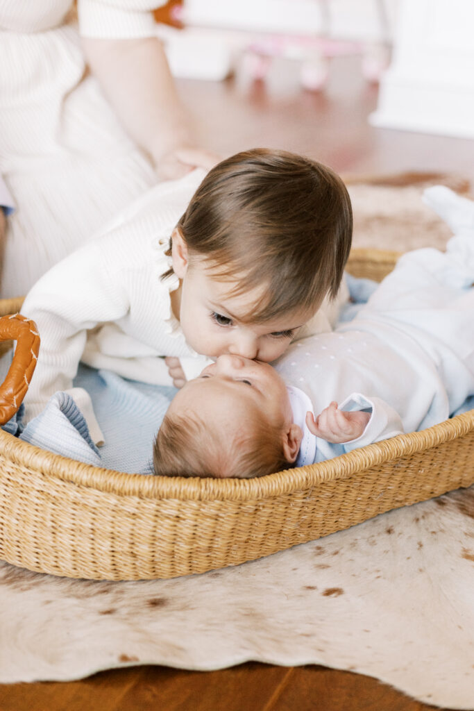 sister kissing newborn baby in moses basket