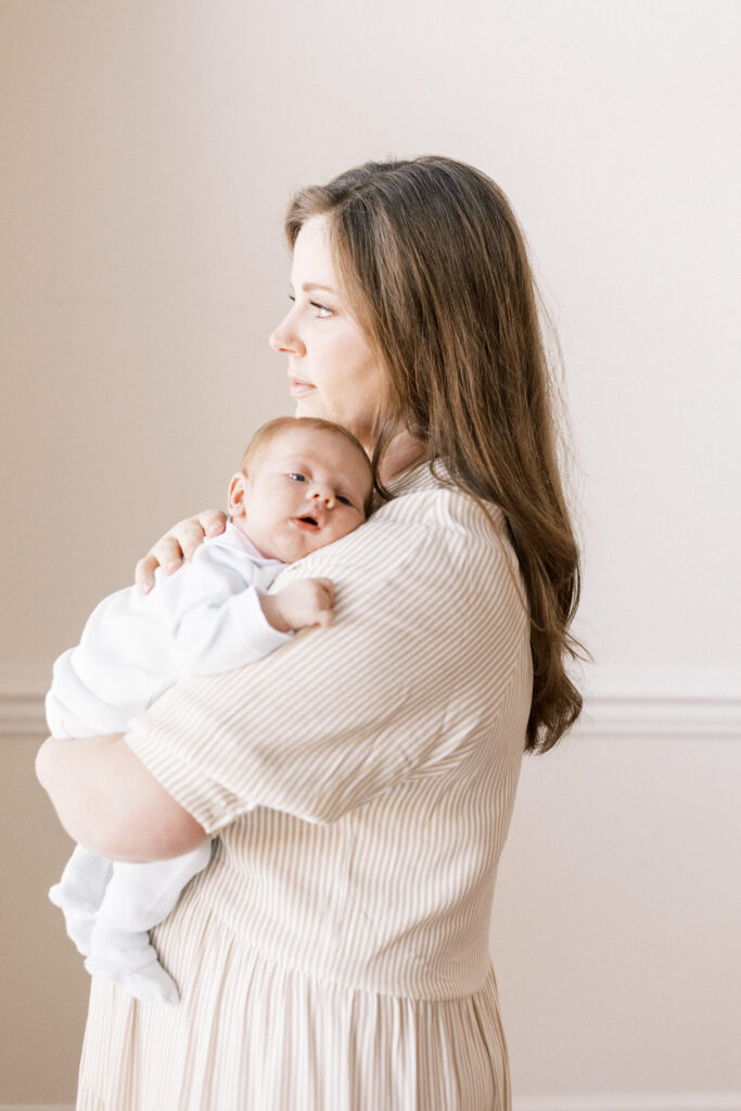 mom looking out window holding newborn baby