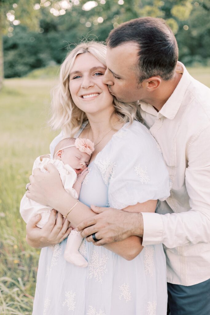husband kissing wife who is holding her newborn baby in peoria illinois
