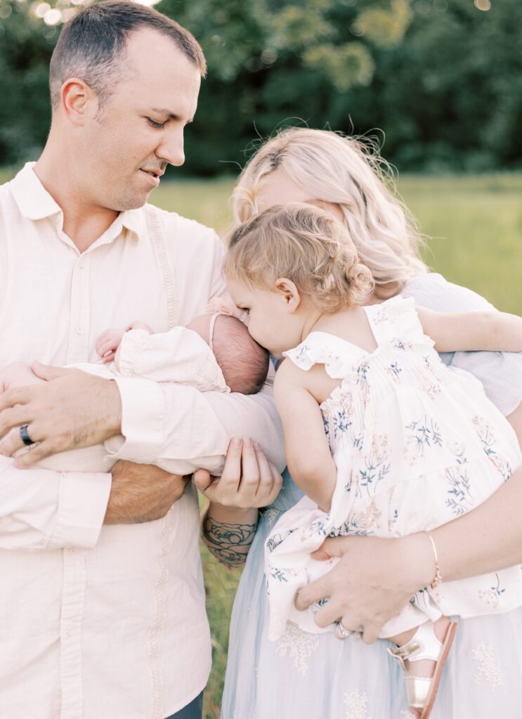 sister leaning over to kiss newborn baby in peoria illinois