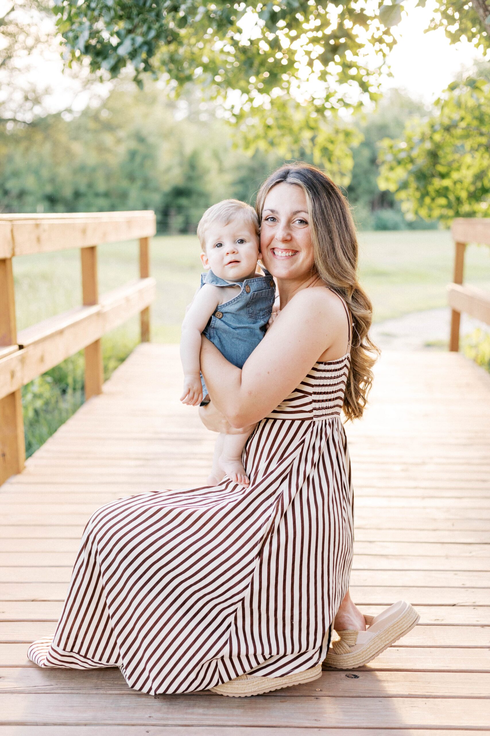 mom kneeling and hugging baby in sunset summer family photos in peoria il