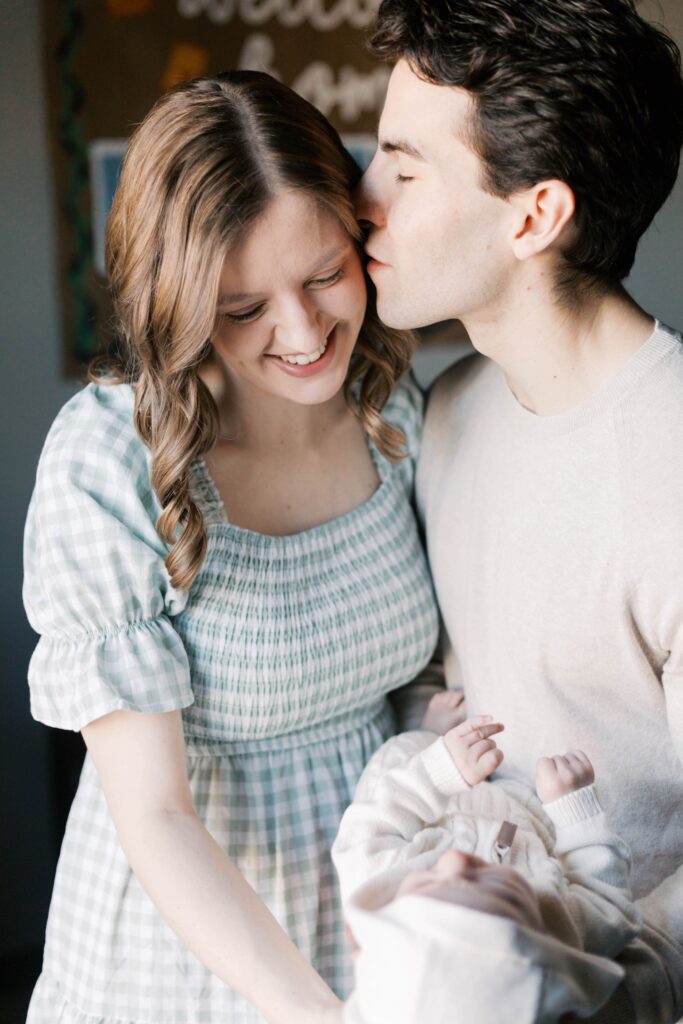 Parents holding their newborn near a small window in a Peoria Illinois apartment during an intimate in-home newborn photography session