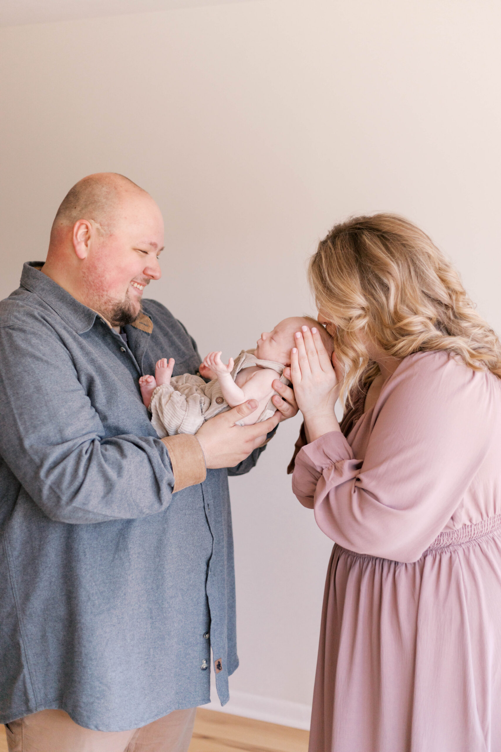 dad looking at baby and mom kissing baby during in-home newborn photos in peoria il