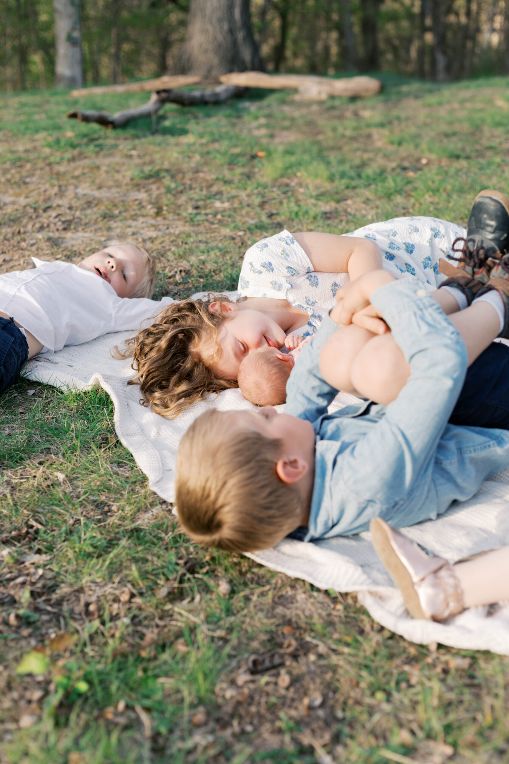 siblings hugging newborn sister on blanket outside during golden hour newborn photos in peoria il