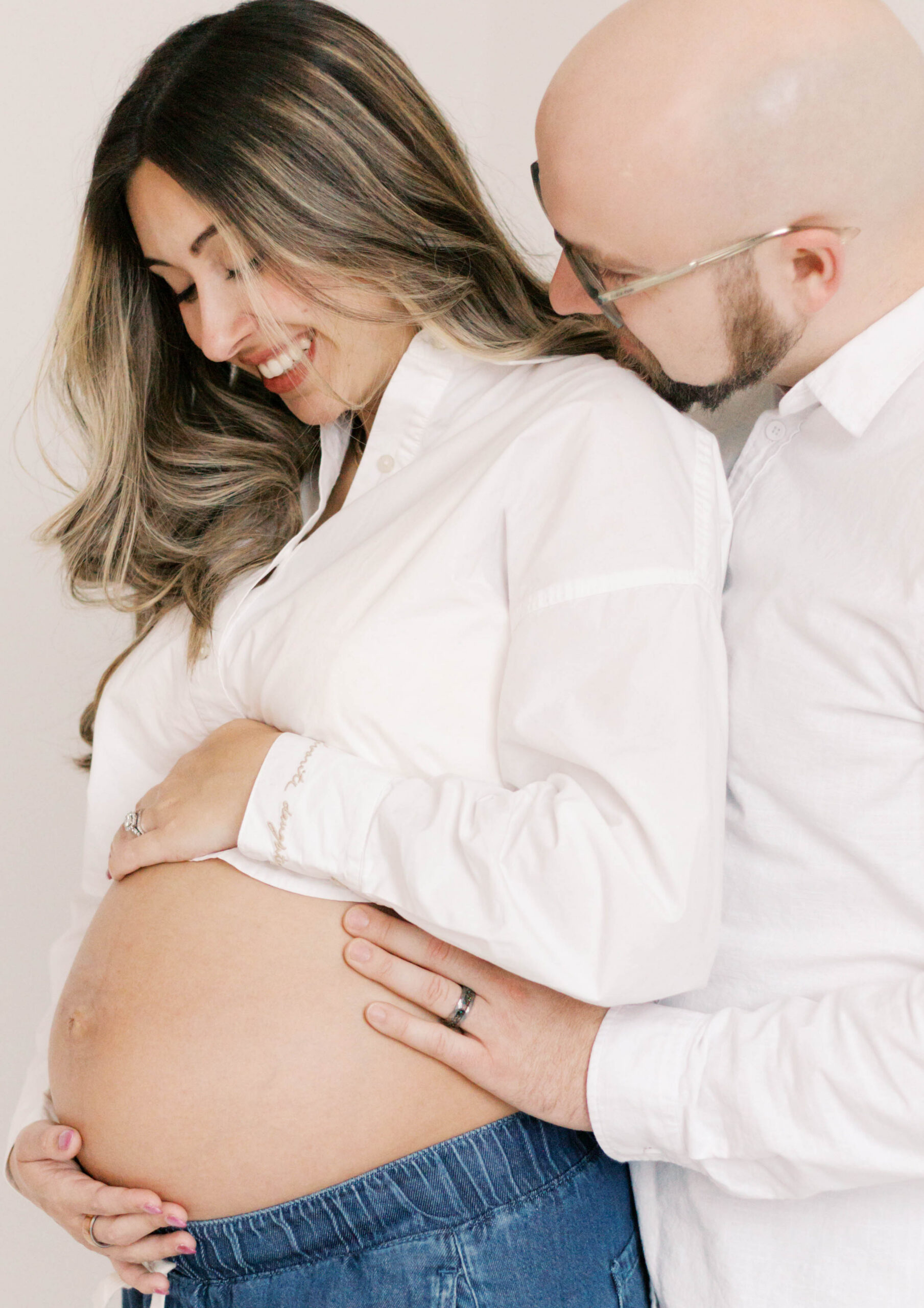 studio maternity photographer peoria il-10 pregnant mom and husband looking at baby bump in white studio maternity photos in peoria il