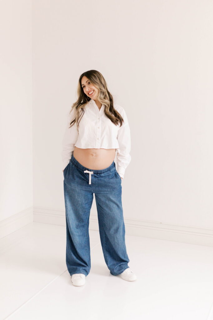 studio maternity photographer peoria il-15 mom standing casually smiling in jeans and white shirt in studio maternity photos peoria il