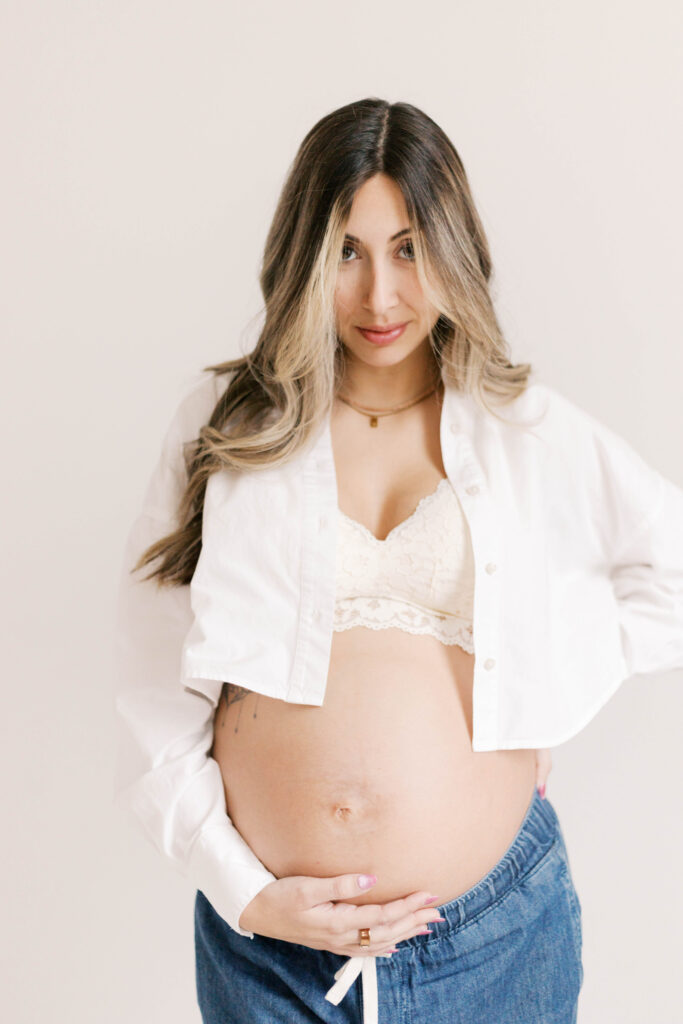 studio maternity photographer peoria il-35 pregnant mom in jeans and white shirt looking at camera in peoria il studio maternity photos