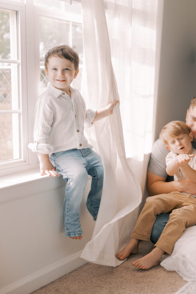 toddler sitting on window sill in newborn photography at home in peoria il