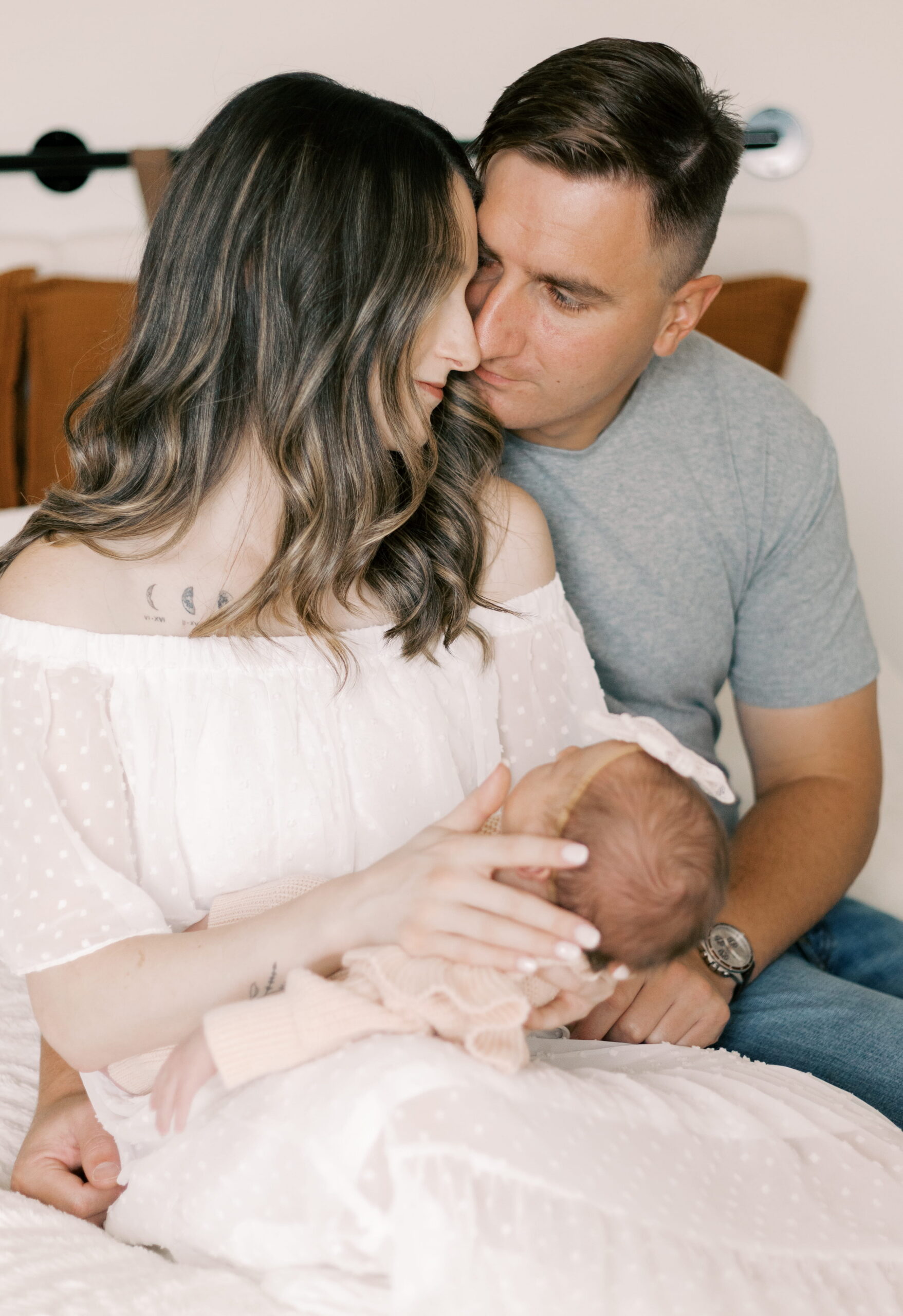 new parents sitting on bed with newborn baby in newborn photography in peoria il
