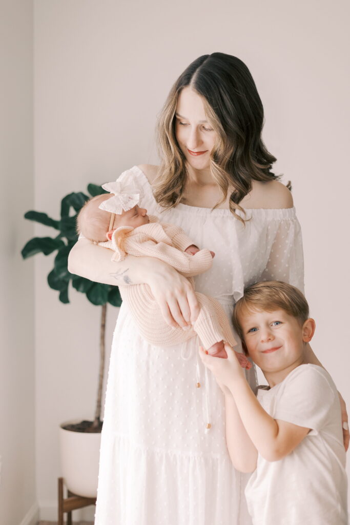 mom stands with new baby and son in home newborn photography in peoria il