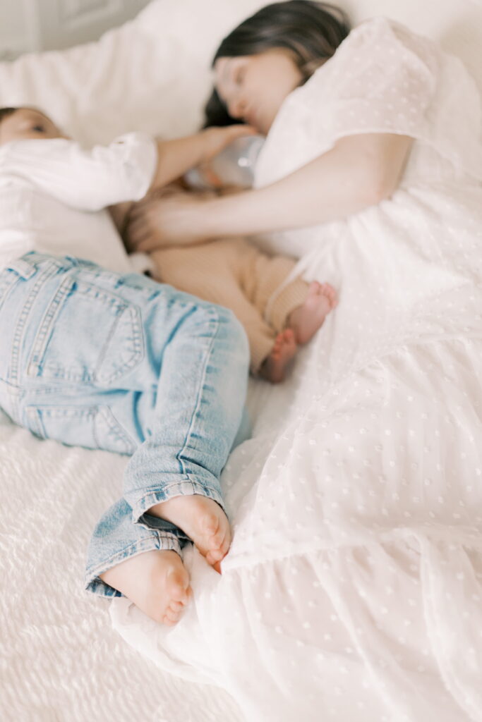 mom laying on bed with toddler and newborn baby in home newborn photography peoria il